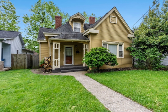 view of front facade with fence, a chimney, a shingled roof, and a front yard