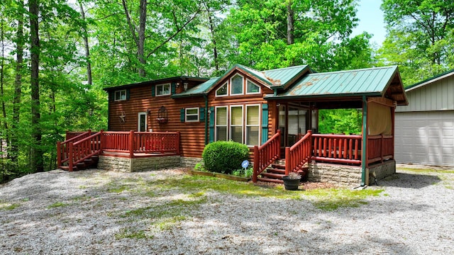 back of house featuring covered porch, metal roof, faux log siding, a garage, and stairs