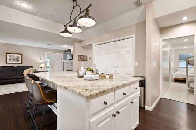 kitchen featuring a kitchen island, light stone countertops, open floor plan, white cabinetry, and dark wood-type flooring