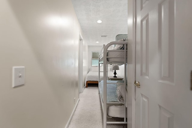 corridor featuring a textured ceiling, visible vents, light colored carpet, baseboards, and recessed lighting