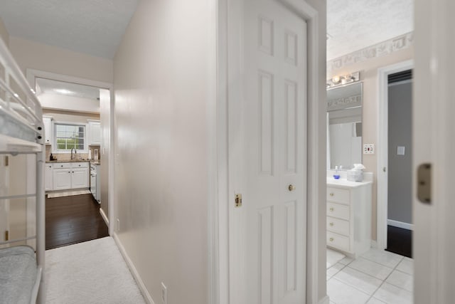hall featuring a textured ceiling, baseboards, a sink, and tile patterned flooring