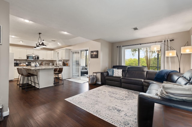 living room with dark wood-style flooring, visible vents, and a raised ceiling