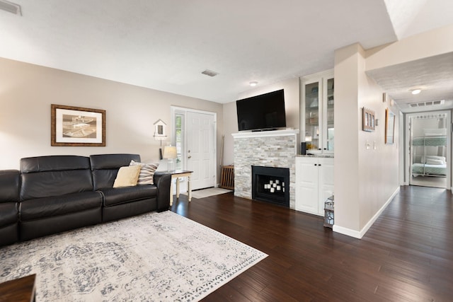living area featuring baseboards, dark wood finished floors, a stone fireplace, and visible vents