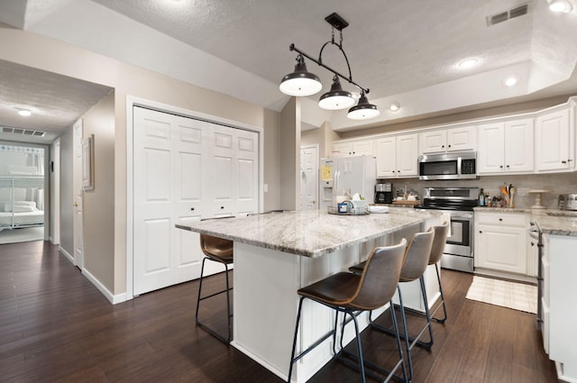 kitchen featuring a breakfast bar, dark wood finished floors, stainless steel appliances, white cabinetry, and visible vents