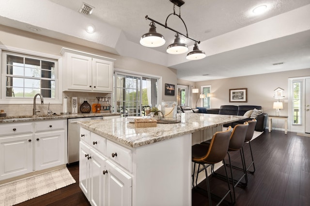 kitchen featuring stainless steel dishwasher, visible vents, open floor plan, a center island, and a sink
