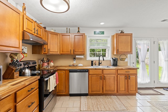 kitchen with a textured ceiling, under cabinet range hood, a sink, light tile patterned floors, and stainless steel appliances