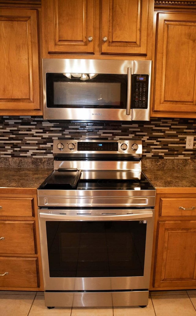 kitchen with dark countertops, appliances with stainless steel finishes, brown cabinets, and light tile patterned flooring