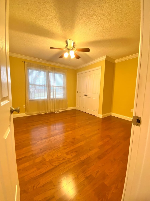 unfurnished bedroom with crown molding, wood finished floors, baseboards, a textured ceiling, and a ceiling fan