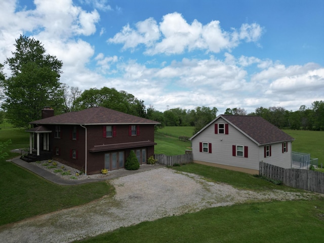 view of side of home with fence, roof with shingles, a chimney, a yard, and driveway
