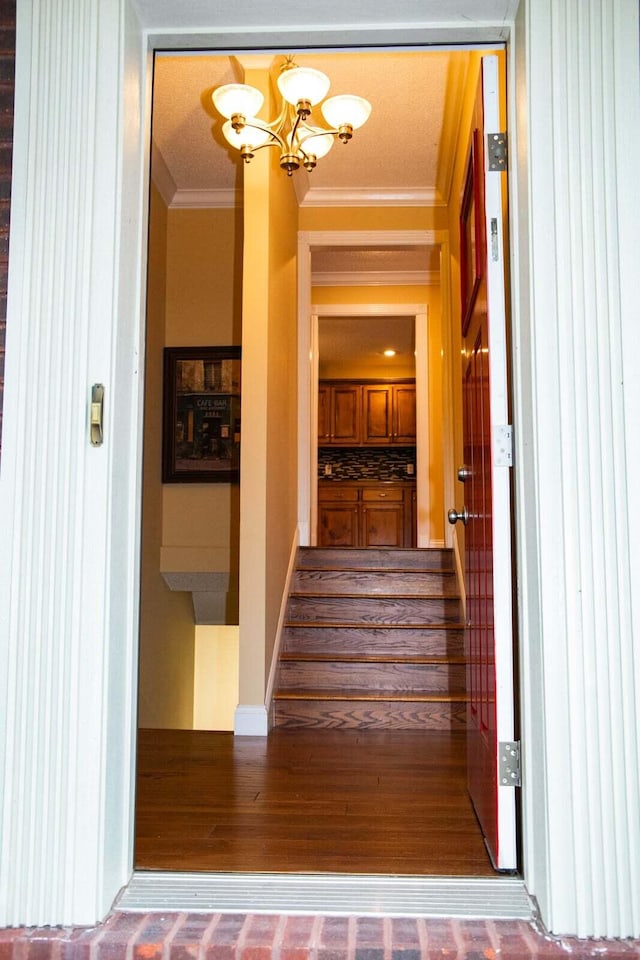 staircase featuring crown molding, wood finished floors, and a notable chandelier