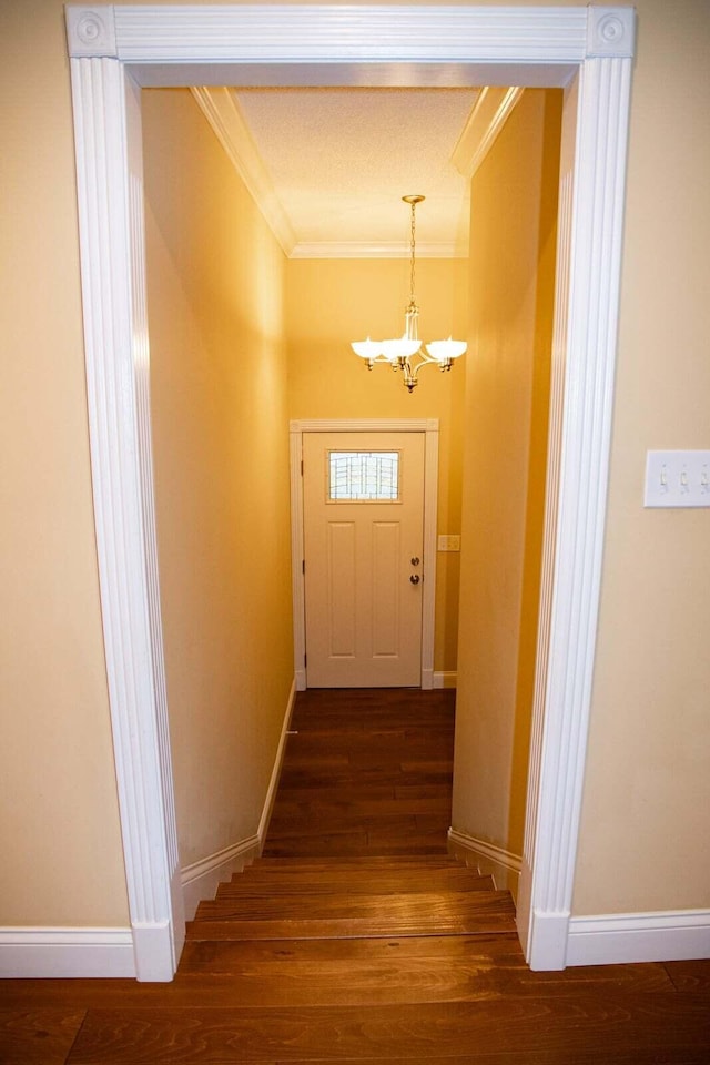 doorway to outside featuring an inviting chandelier, ornamental molding, baseboards, and wood finished floors