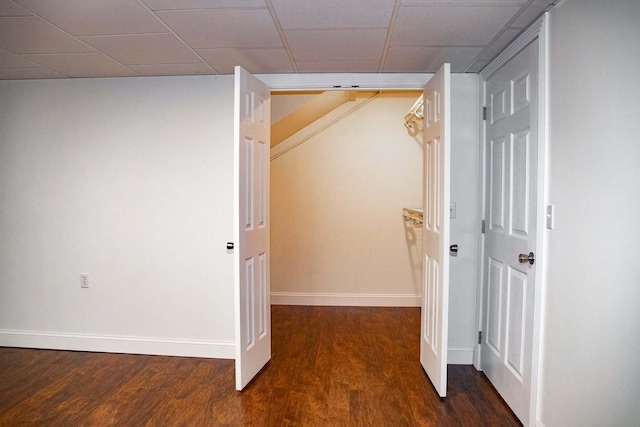 corridor featuring baseboards, a paneled ceiling, and wood finished floors