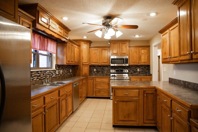 kitchen with a ceiling fan, dark countertops, brown cabinets, a sink, and stainless steel appliances
