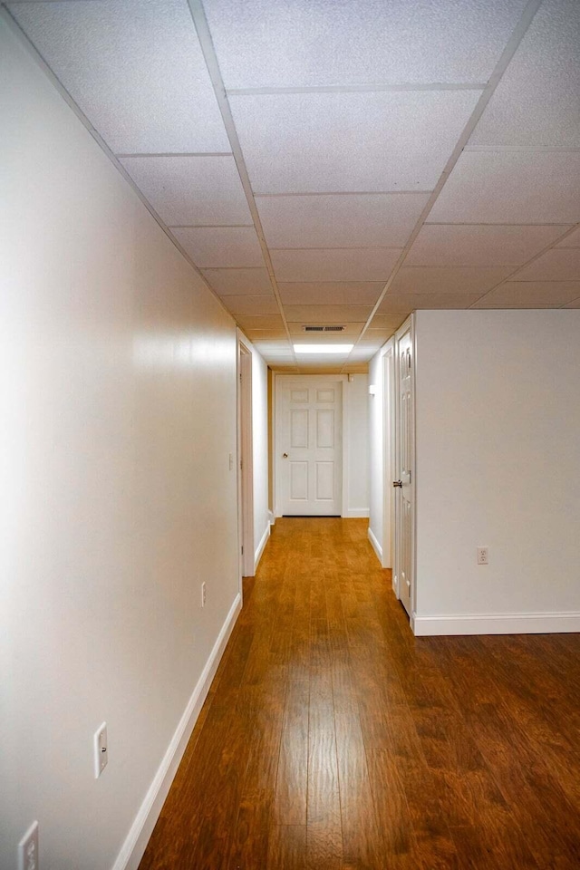 hallway with a paneled ceiling, baseboards, and wood finished floors