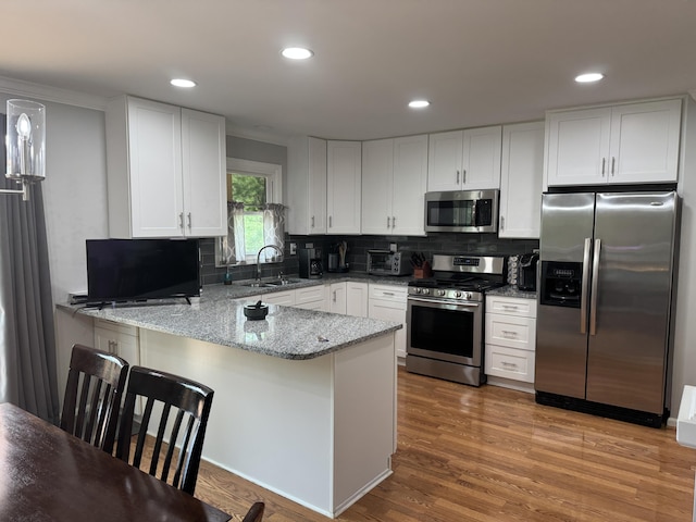 kitchen featuring light stone counters, a sink, stainless steel appliances, white cabinetry, and a peninsula