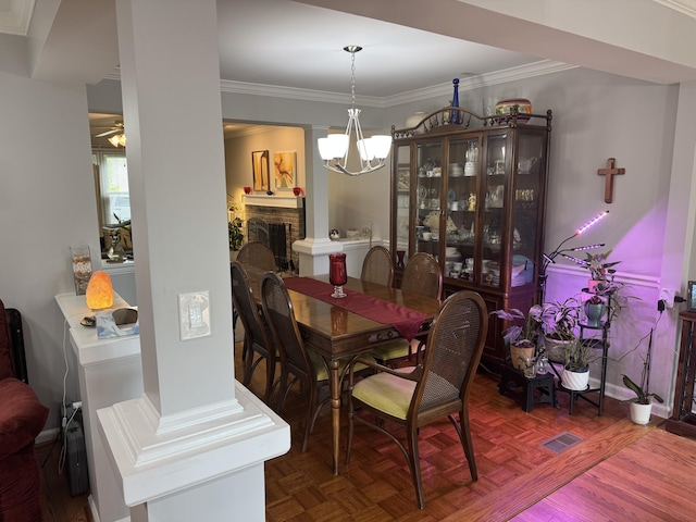 dining area with crown molding, a brick fireplace, ceiling fan with notable chandelier, and visible vents