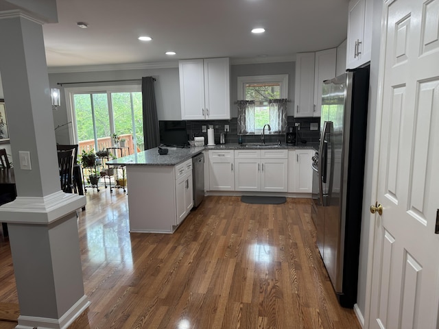 kitchen featuring a sink, white cabinets, a peninsula, ornamental molding, and stainless steel appliances