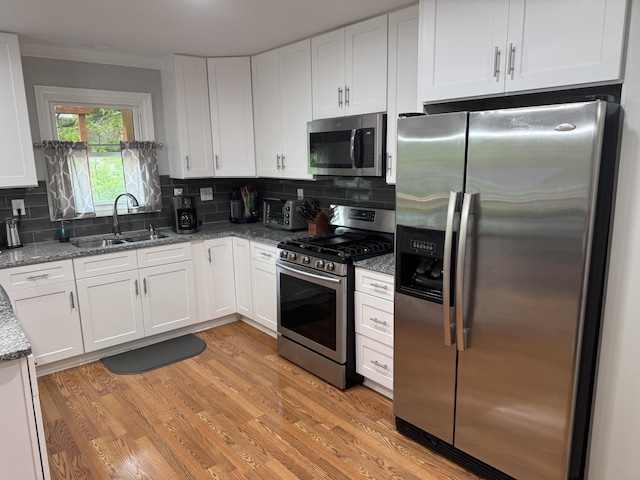kitchen with appliances with stainless steel finishes, tasteful backsplash, a sink, white cabinets, and ornamental molding