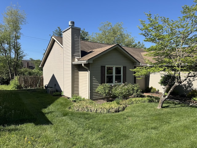 view of side of property with a lawn, central AC, a chimney, and a shingled roof