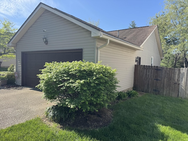 view of home's exterior with concrete driveway, an attached garage, fence, and a shingled roof
