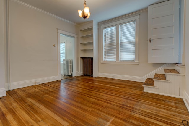unfurnished living room with radiator, wood finished floors, baseboards, built in shelves, and a notable chandelier
