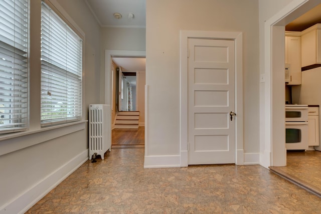 hallway with radiator heating unit, baseboards, and ornamental molding