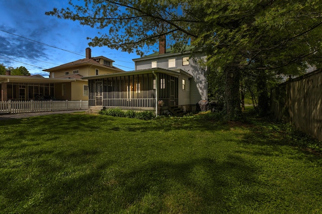 back of house with a lawn, fence, a chimney, and a sunroom