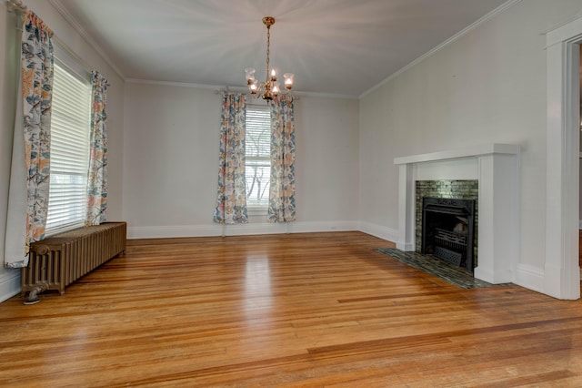unfurnished dining area featuring an inviting chandelier, crown molding, radiator, a fireplace, and light wood-type flooring