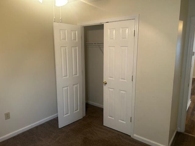 unfurnished bedroom featuring baseboards, a closet, and dark carpet