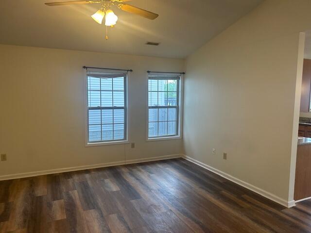 spare room featuring visible vents, dark wood-style flooring, lofted ceiling, baseboards, and ceiling fan
