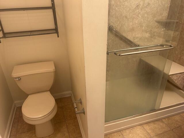 bathroom with toilet, baseboards, a shower stall, and tile patterned flooring