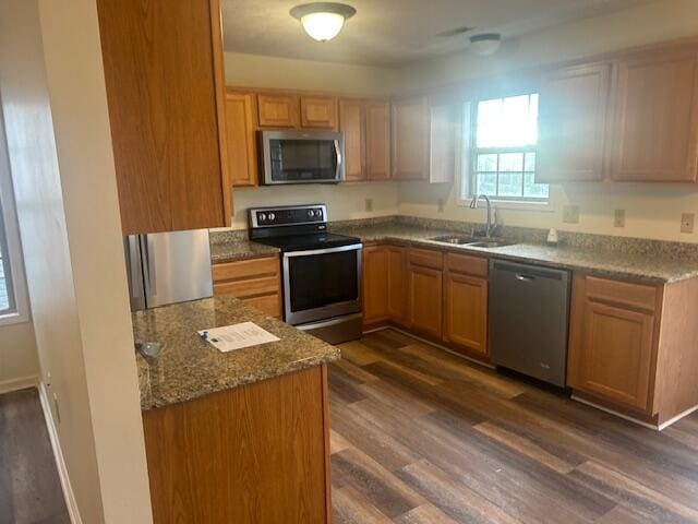 kitchen featuring stone countertops, appliances with stainless steel finishes, a sink, and dark wood finished floors
