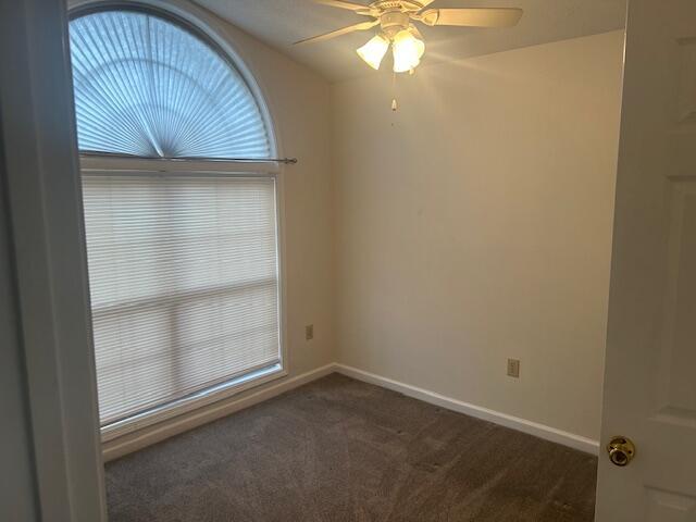 empty room featuring baseboards, a ceiling fan, and dark carpet