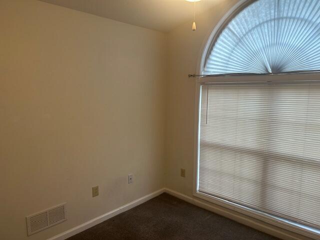 spare room with visible vents, baseboards, and dark colored carpet