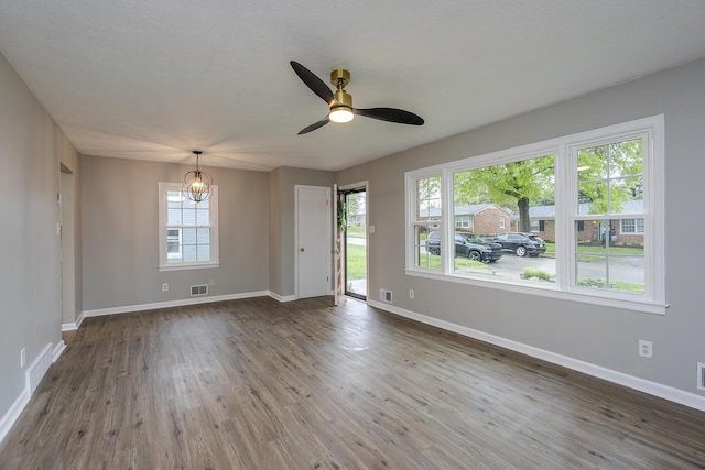 unfurnished room with visible vents, baseboards, ceiling fan with notable chandelier, and wood finished floors