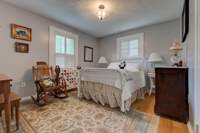 bedroom featuring baseboards, a textured ceiling, and light wood finished floors