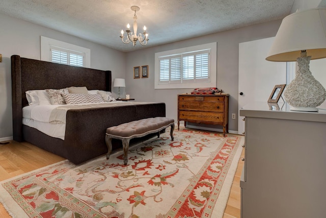 bedroom featuring a textured ceiling, an inviting chandelier, multiple windows, and light wood-style flooring