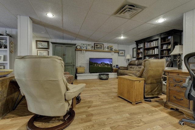 living room featuring a fireplace, a drop ceiling, light wood-style flooring, and visible vents