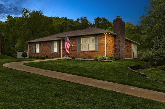 ranch-style home featuring a chimney, brick siding, and a front yard