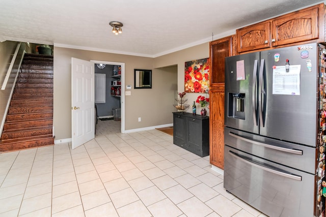 kitchen featuring stainless steel refrigerator with ice dispenser, crown molding, brown cabinets, light tile patterned floors, and baseboards