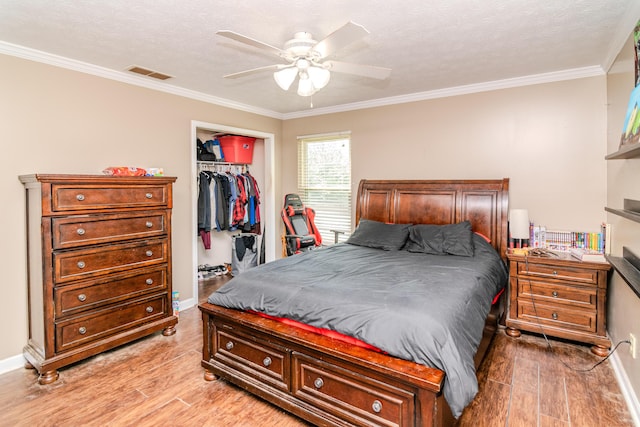 bedroom featuring visible vents, ornamental molding, a closet, a walk in closet, and light wood-type flooring