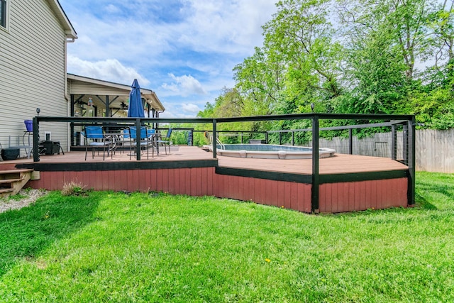 deck featuring a jacuzzi, fence, and a yard