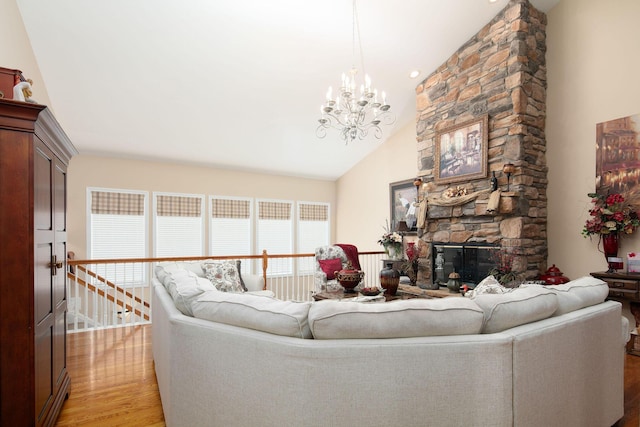 living area featuring light wood finished floors, a chandelier, high vaulted ceiling, and a stone fireplace