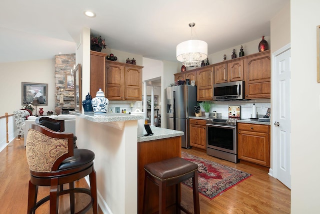 kitchen with appliances with stainless steel finishes, a kitchen breakfast bar, a peninsula, light wood-style floors, and brown cabinetry