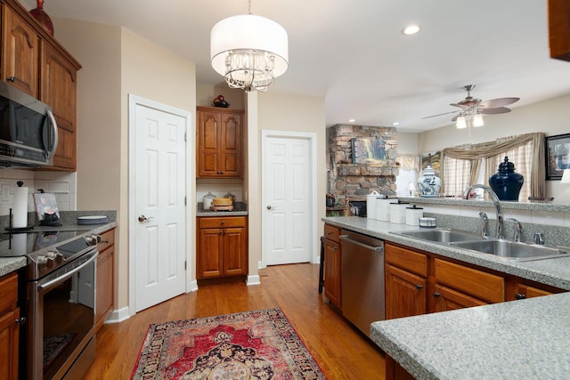 kitchen with appliances with stainless steel finishes, a sink, decorative backsplash, a ceiling fan, and light wood finished floors