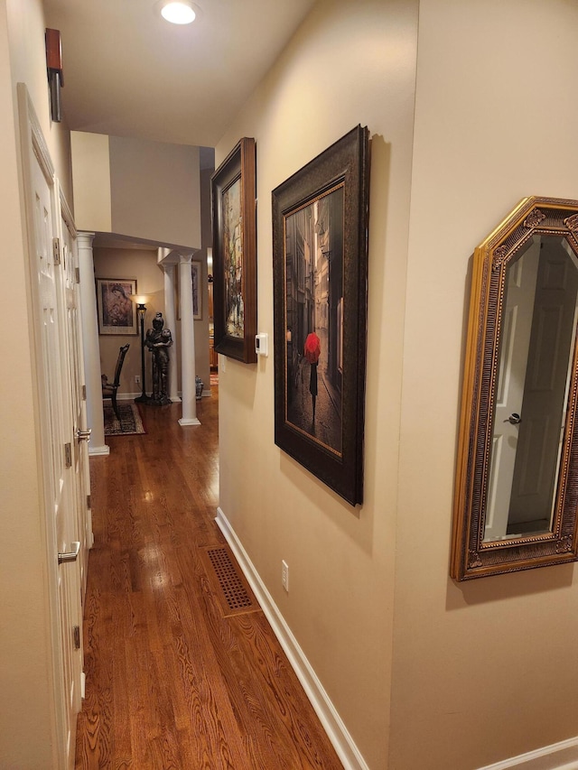 hallway featuring ornate columns, dark wood-style flooring, and baseboards