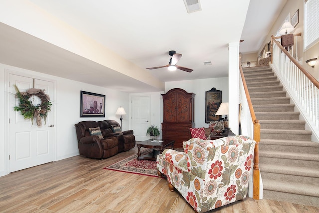 living area with stairs, light wood-style floors, a ceiling fan, and ornate columns