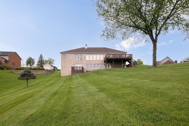 rear view of house featuring a lawn, a wooden deck, a chimney, and brick siding