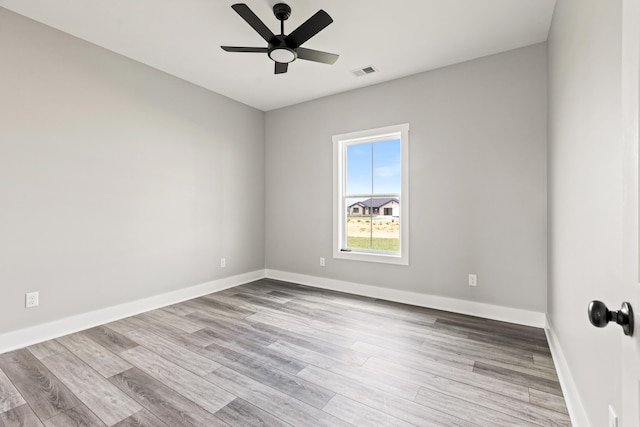 empty room with baseboards, a ceiling fan, wood finished floors, and visible vents