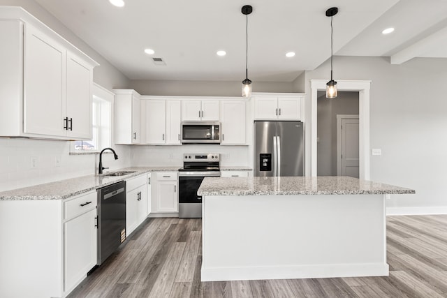 kitchen featuring a sink, light wood-style flooring, stainless steel appliances, tasteful backsplash, and a kitchen island